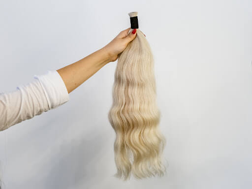 Image of someone holding long, blonde hair extensions Image of someone holding long, blonde hair extensions