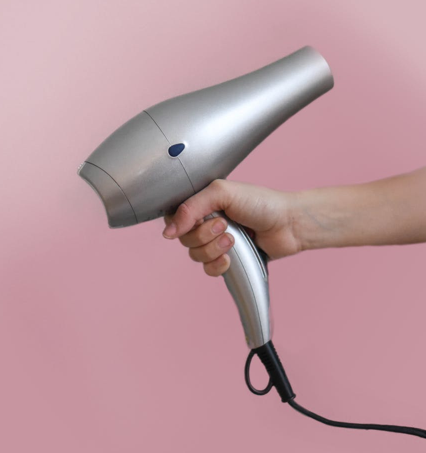 Hand holding a silver blow dryer against a pink background
